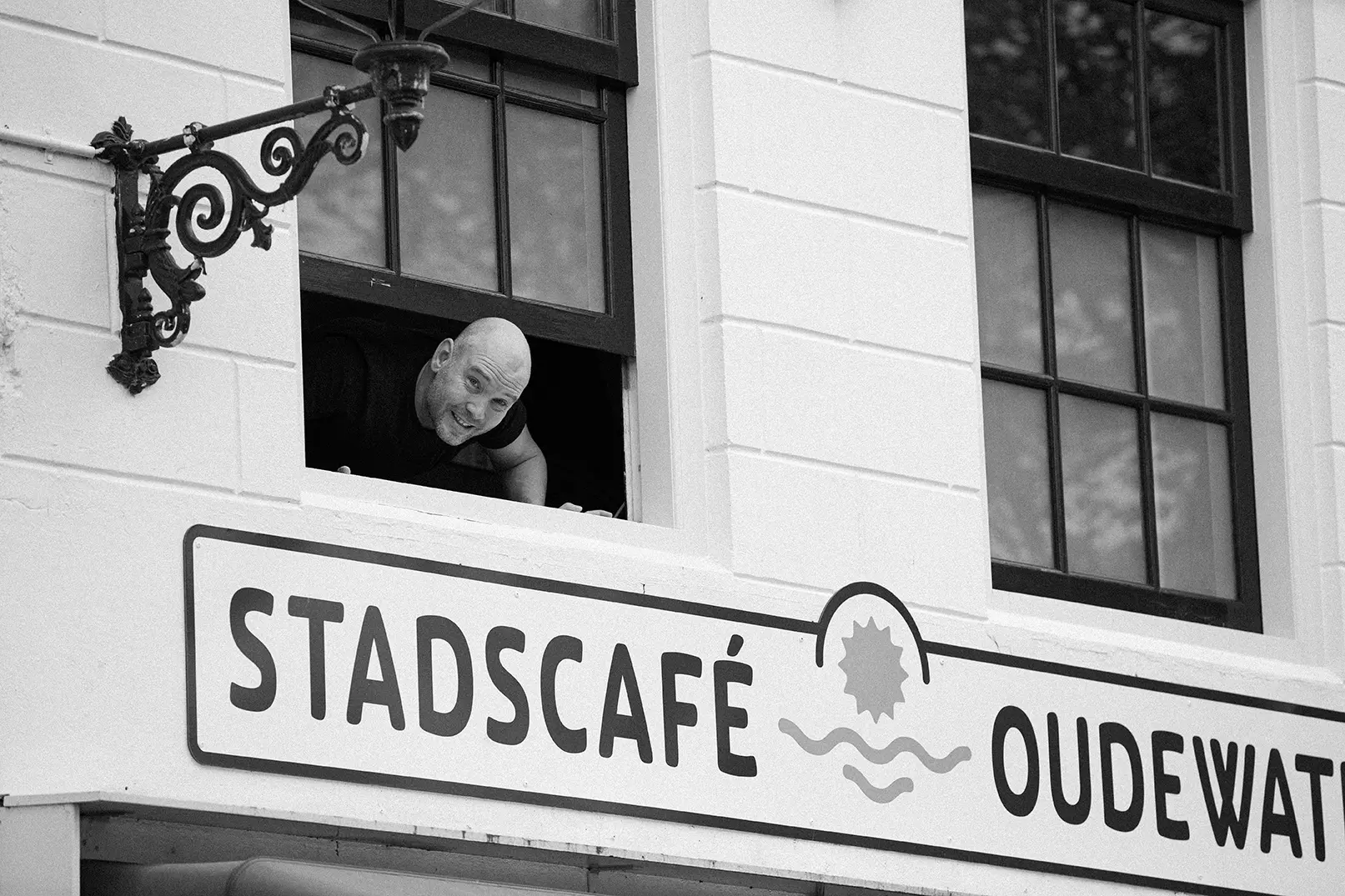 Medewerker leunt lachend uit het raam boven de gevelnaam van Stadscafé Oudewater