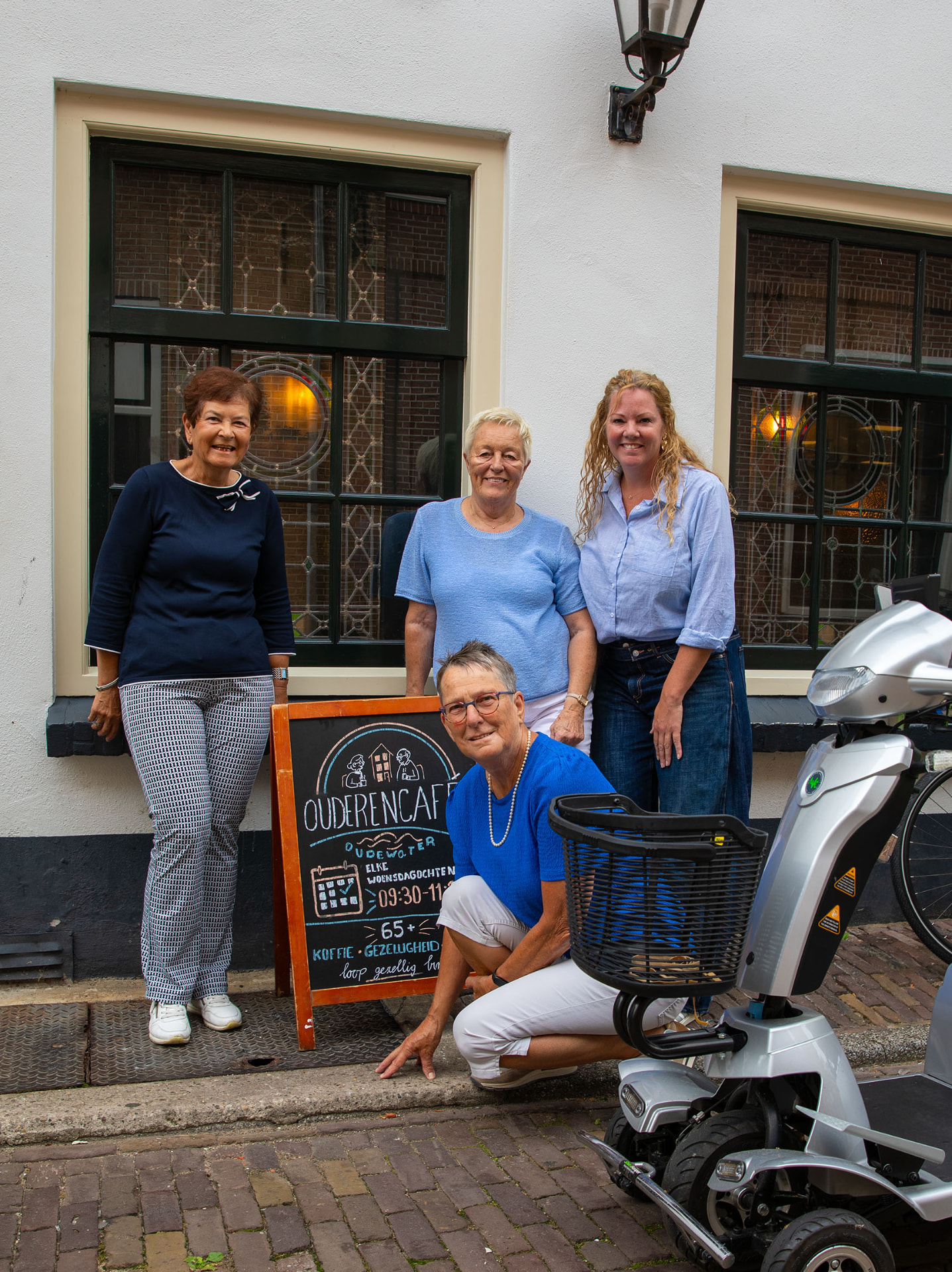 Vier vrijwilligers van het Ouderencafé bij het krijtbord voor het Stadscafé